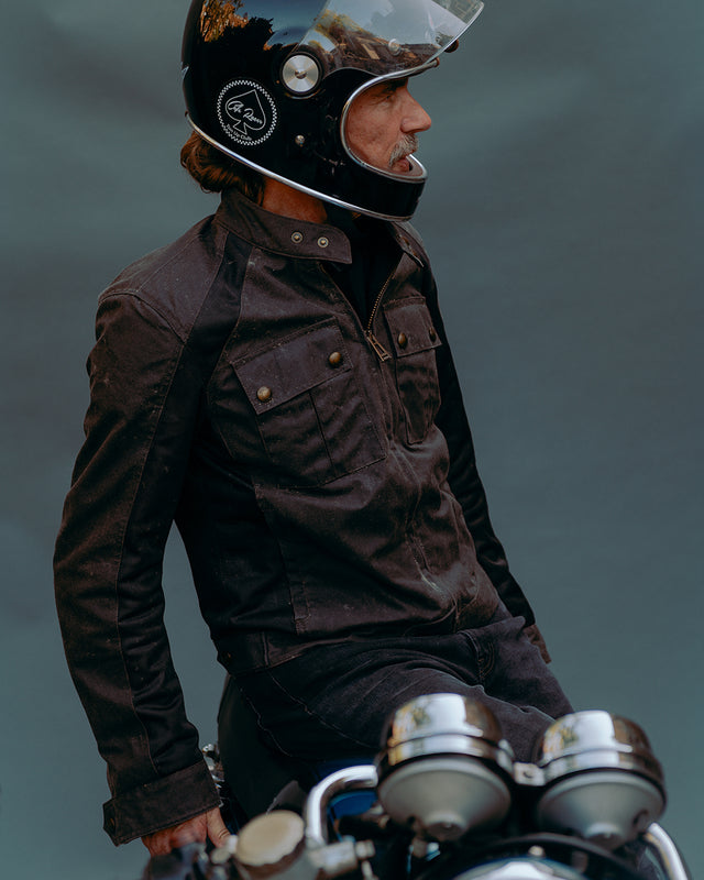 Man with black full face helmet and Belstaff waist long jacket sitting on a motorcycle 