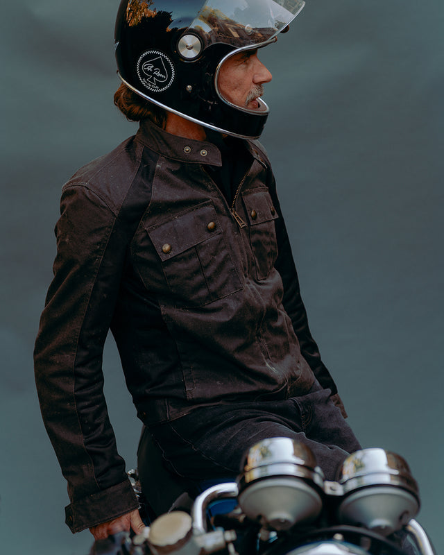 Man with black full face helmet and Belstaff waist long jacket sitting on a motorcycle