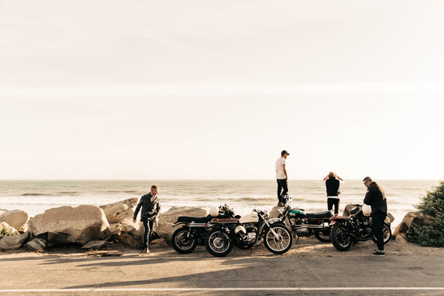 Four guys with retro scrambler motorcycles looking out over the water.