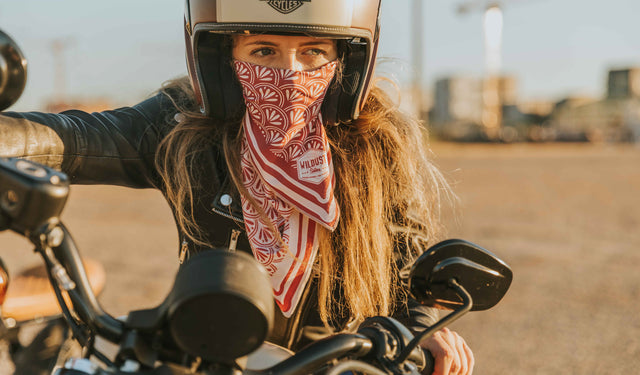 Female motorcycle rider with open face helmet, black leather jacket and burgundy scarf.