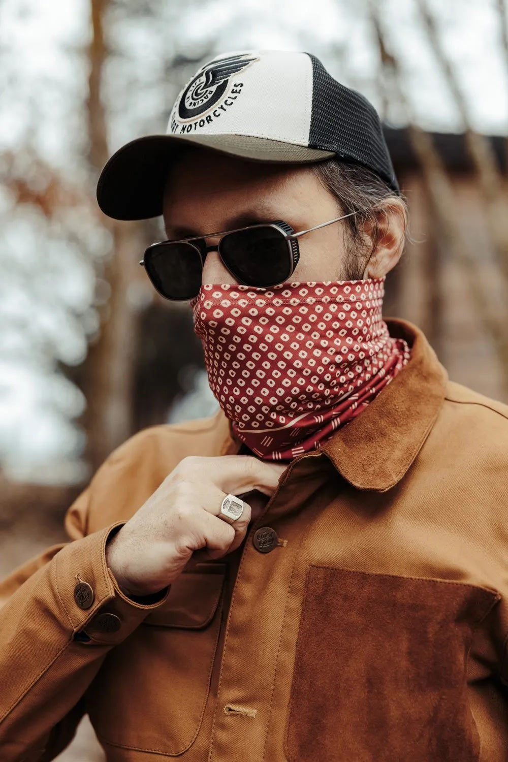 Man in sunglasses and cap is wearing a red neckwarmer with white dots.