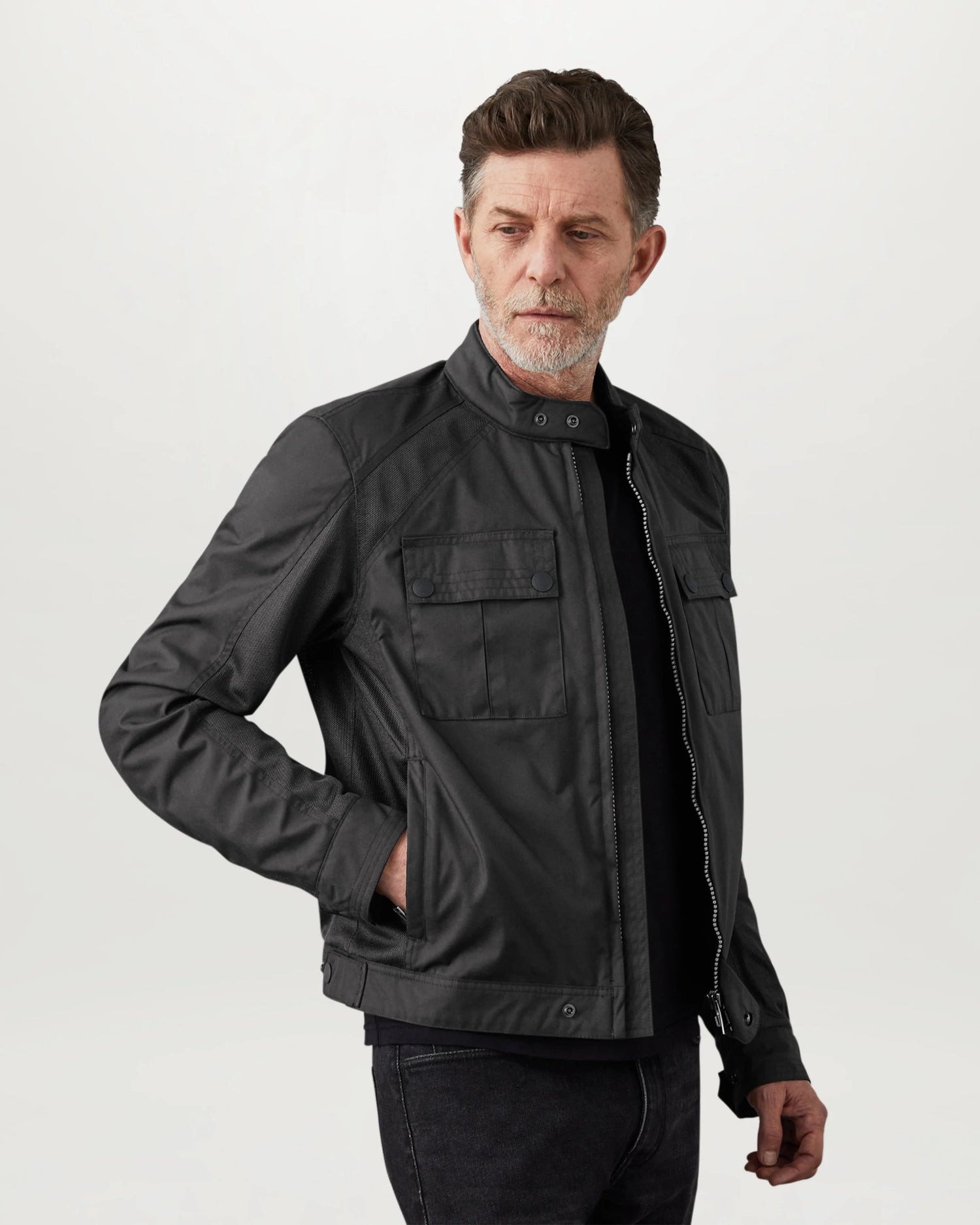 Man wearing a black Belstaff Temple motorcycle jacket with mesh ventilation panels and chest pockets.