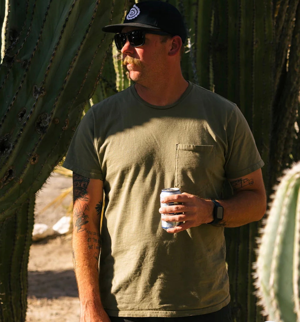 Mustasched man in black cap and sunglasses holding a can of soda while wearing a pocket t-shirt.