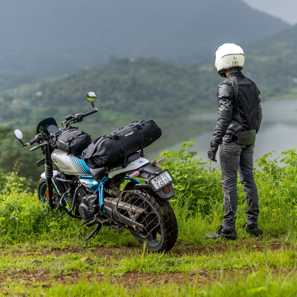 Man in motorcycle helmet and leather jacket standing beside motorcycle equipped with tail and tank luggage. 