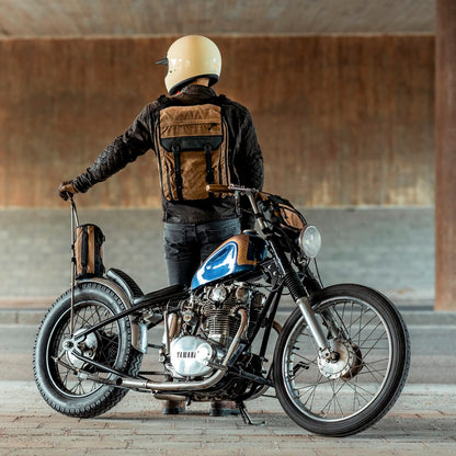 Motorcycle rider with brown backpack standing behind a Yamaha chopper styled motorcycle.