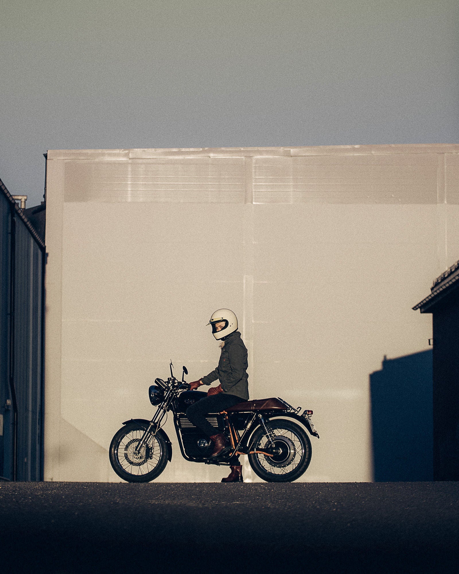 Motorcycle rider on electric motorcycle parked infront of a white  wall.