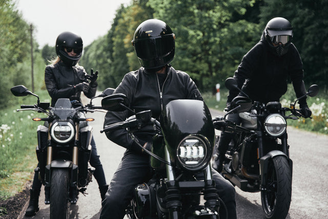 Three motorcycle riders in black motorcycle gear sitting on black motorcycles.